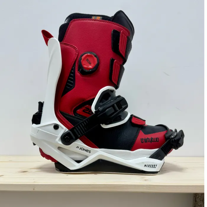 A snowboard boot strapped into a rear-entry binding on a wooden bench
