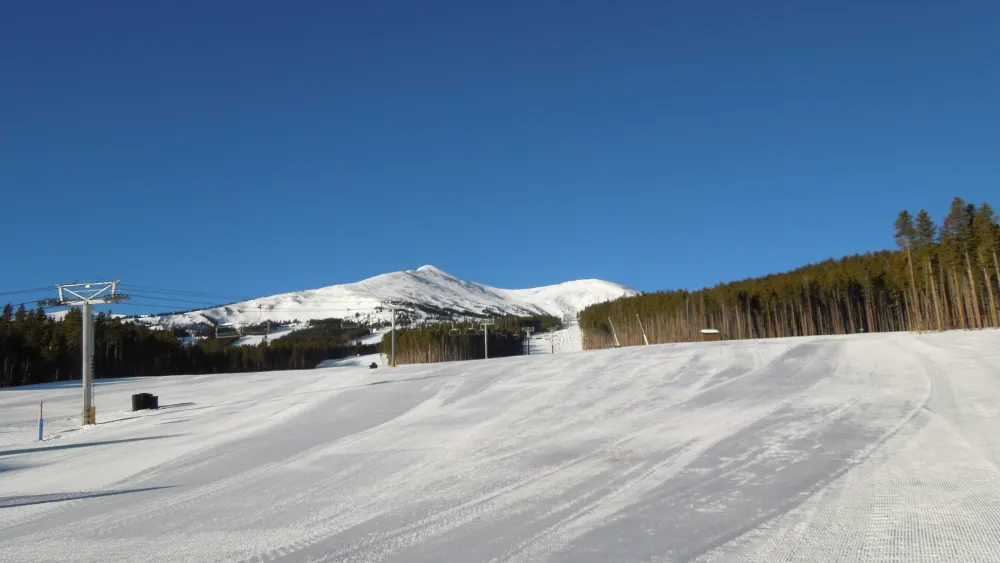 A groomed run and lift line at the base of Breckenridge with Peak 8 beyond the trees on a clear morning