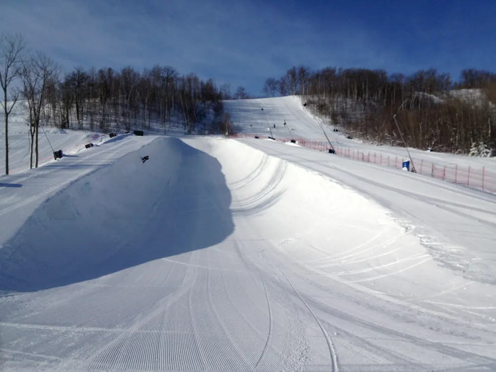 A freshly groomed halfpipe on a sunny day with a lone rider dropping in at the far end