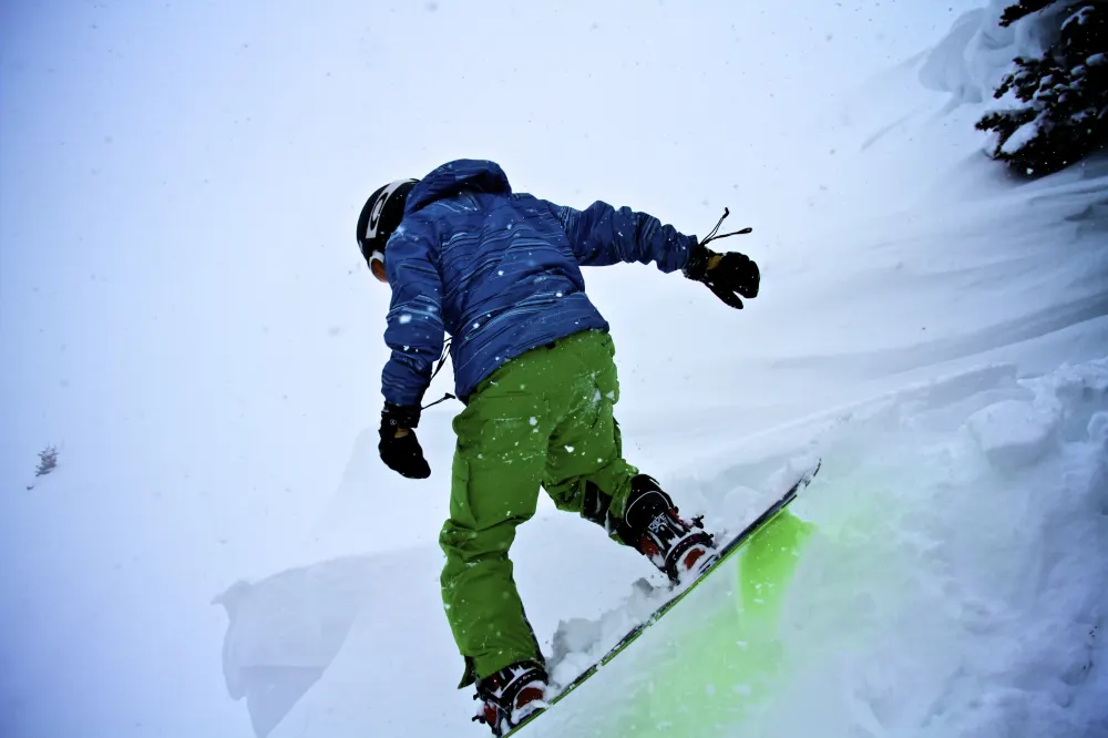 A snowboarder seen from behind dropping into deep powder during a snowstorm on Berthoud Pass